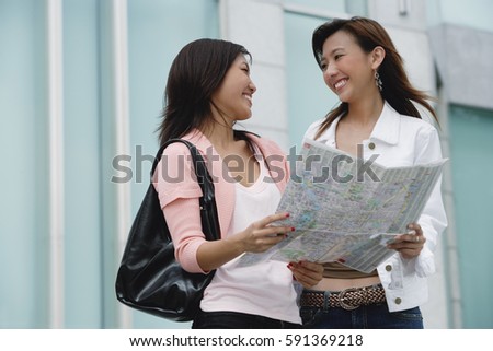 Two women with map, smiling at each other