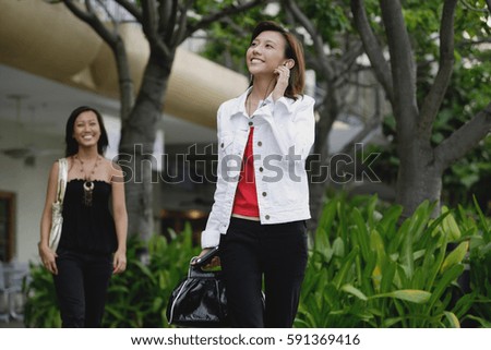Woman walking, using mobile phone, another woman in the background