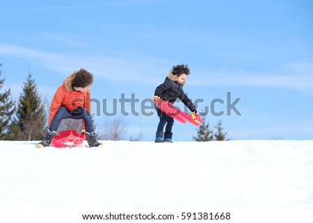 Happy young brothers on sled walking in winter outdoors

