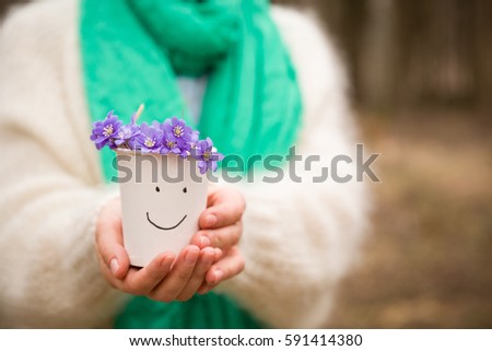 Woman holding beautiful snowdrops in a paper cup. first spring flowers in a forest. Wild flowers. spring concept.