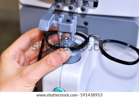 Female optician measuring and preparing glasses on the latest digital device in optical store  Royalty-Free Stock Photo #591438953