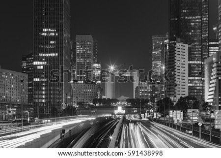 Night cityscape with modern buildings in Paris business district La Defense with dynamic traffic and car lights. Glass facade skyscrapers. Concept of economics, finances. Copy space. Black and white
