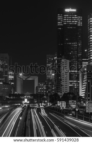 Night cityscape with modern buildings in Paris business district La Defense with dynamic traffic and car lights. Glass facade skyscrapers. Concept of economics, finances. Copy space. Black and white