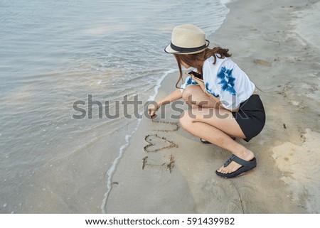 Asia girl writing word "I Love You" in sand on beach