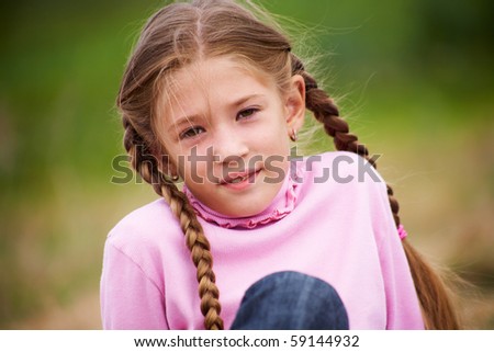 portrait of little girl with pigtails smiling at the camera against  background of green