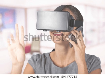 Woman talking on mobile phone while using virtual reality headset in office
