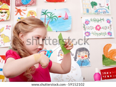  Child with scissors cut paper in play room. Preschool.