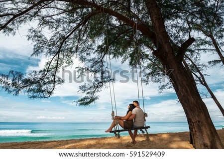 Couple in love on a swing by the sea. Couple in love on an island off the coast. Honeymoon. Couple by the sea. Man and woman travel to beautiful places. Honeymoon trip. Relax on the island. In love Royalty-Free Stock Photo #591529409