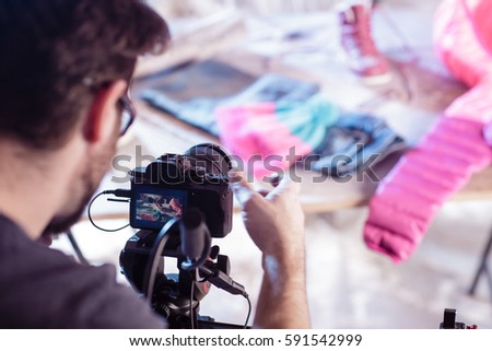 Cameraman is looking at the camera display on the set in studio with blurred colorful background. Moment from shooting with preparation of the shot. Color toned image.
