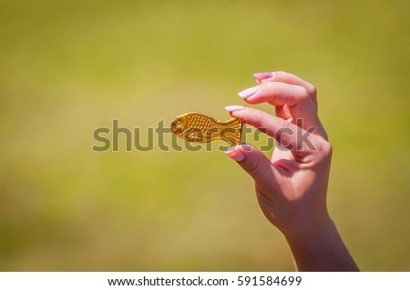 Girl's hand with a nice manicure holding a golden fish chocolate candy. An abstract image of auspiciousness, good fortune, luck, freedom and happiness.