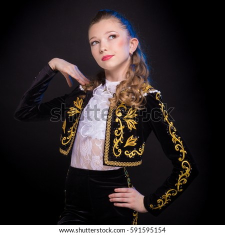Portrait of teen girl in a suit of black bullfighter jumping, dancing and posing on a dark background in the studio