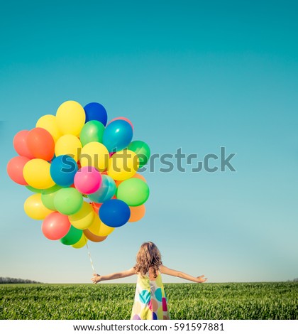 Happy child playing with bright multicolor balloons outdoor. Kid having fun in green spring field against blue sky background. Summer vacation and travel concept