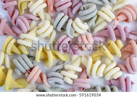 Curly and twisted pasta shapes on a cutting board in various colors of pink, yellow, green and white