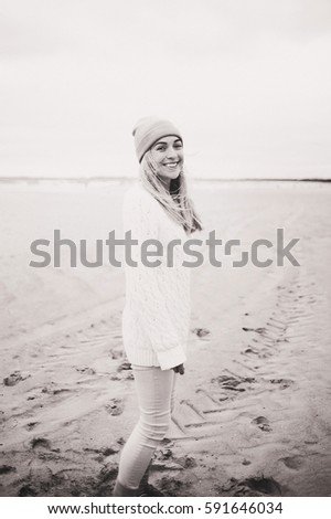 Young happy woman in white cozy knitted sweater posing near wooden wall at the seaside of Baltic sea. Seaside background.