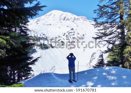 Snowshoer enjoys the view and snaps a picture of Mount Rainier on a beautiful winter day at the national park in Washington state.