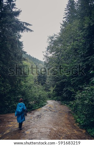 The girl is on the road in the mountains, beautiful landscape and large green trees