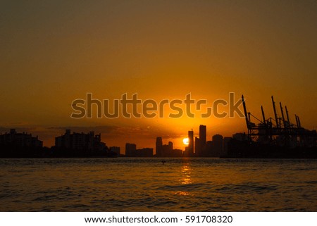 Orange sunset over city scape and lake with a boat passing by