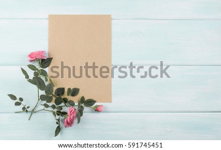 Wooden background with roses and empty kraft eco paper with place for text. Top view. Flat design.