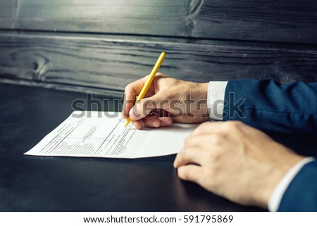 Man the lawyer signs documents with a pen making the signature sitting at the desk on a dark background. The concept of insurance and legal solutions