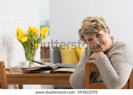 Smiling senior woman sitting on a chair and old photo album laying on a table behind her