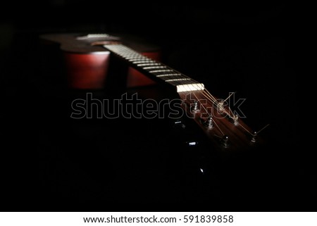 A shaded picture of a guitar. It lies in the dark with only a part visible under small amount of light. 