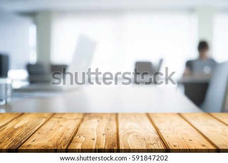 Empty wooden desk space over blurred office or meeting room background. Product display.
