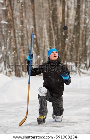 Hockey player poses standing on one knee  and throwing puck up at outdoor skating rink in park.