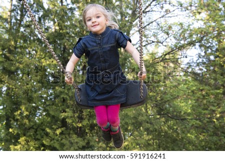 Little child blond girl having fun on a swing outdoor. Summer playground. Girl swinging high