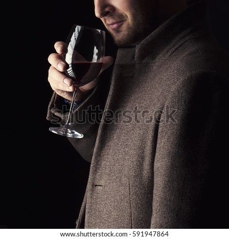 A glass of red wine holding by man wearing spring coat,  smelling red wine before tasting and drinking it. Low key portrait.
