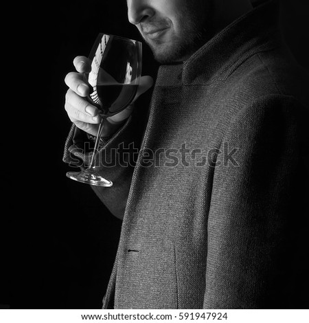 A glass of red wine holding by man wearing spring coat,  smelling red wine before tasting and drinking it. Low key portrait. Black and white