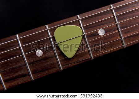 Green guitar pick on the fingerboard Royalty-Free Stock Photo #591952433