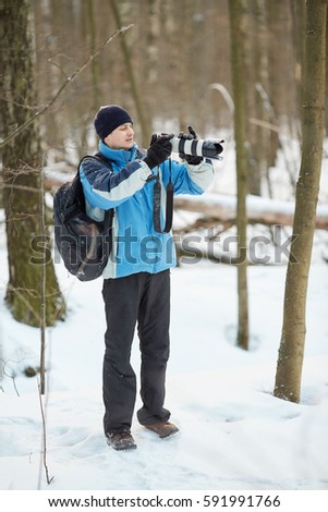 Young man takes pictures standing in winter forest during snowfall.