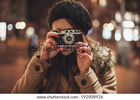 Hipster girl with retro camera taking photos in the night city street