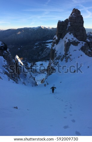 View of a mountaineering skier while climbing the mountain slope to reach the summit, with panorama of snowy mountain range in background, Mount Carega, Italy