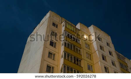 Orange nine-storey residential building on a blue night sky. One window glows in the dark.