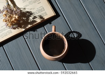Cup of coffee, dry flowers and open book on wooden table. Romantic, retro backgroun, hard light