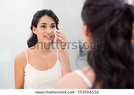 Healthy fresh girl removing make up from her face with cotton pad. Smiling girl cleaning her face in bathroom. Beautiful healthy woman making scrub on her face. Royalty-Free Stock Photo #592066556