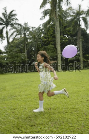 Girl running in park, purple balloon flying behind her