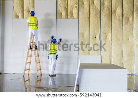 Workers are assembly gypsum wall. Plasterboard is under construction using wooden ladder. Royalty-Free Stock Photo #592143041