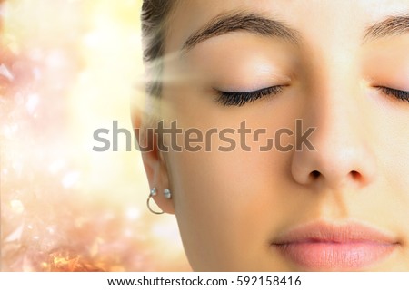 Extreme Close up face shot of young woman with eyes closed.Girl doing mental exercise against bright background with light beam. Royalty-Free Stock Photo #592158416