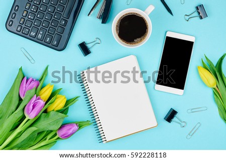 Work desk with notebook, phone, keyboard, coffee and flowers. Top view of working accessories with tulips