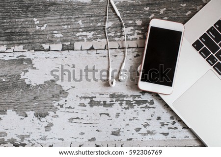 Phone with headphones on wood background with laptop