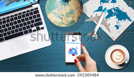 Traveling concept. Woman searching for destination on modern phone. Top view of blue desk with laptop, globe, airplane  and other stuff