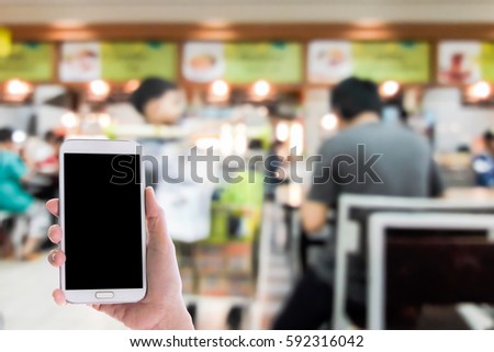 Girl use mobile phone, blur image of father and son eating at food center inside the mall as background.