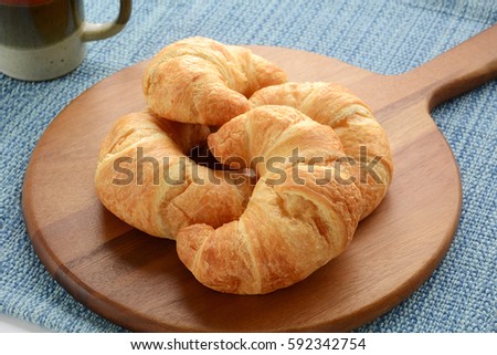 Fresh buttery croissants with tea on rustic wooden board on blue background