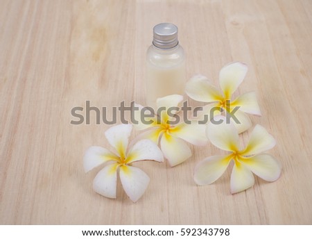 Bottle with aroma oil and tropical flowers Frangipani on wooden background.