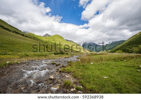 River flowing from the Shkhara Glacier in Caucasian mountains, Upper Svaneti, Georgia. Green meadows and early snow.