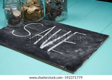 Savings, coins in glass jar with text written on black board.
