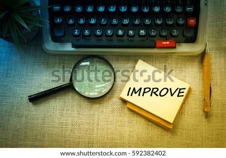 IMPROVE wording on notebook with typewriter ,pen and 
magnifying glass on wooden table. Motivation and positive wishes concept
