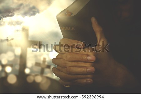 Picture of christian person praying to the GOD while holding a bible with crucifix symbol on the background